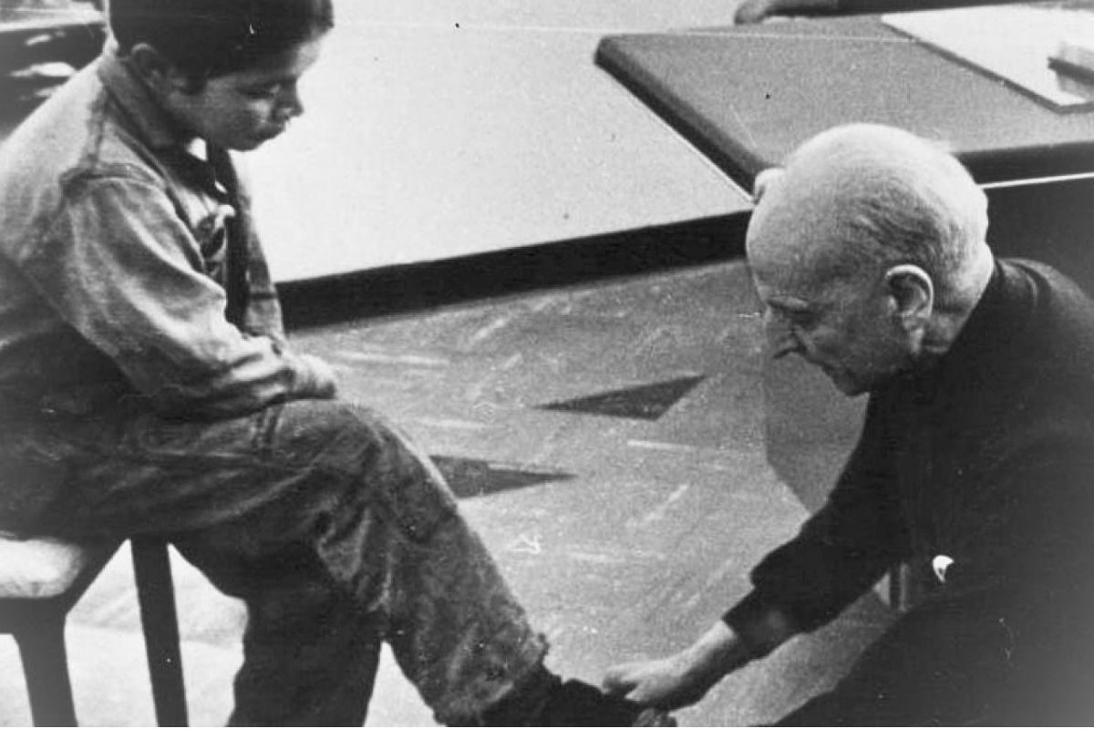 Black-and-white photograph of Father Pedro Arrupe bending towards the foot of a child seated on a chair.