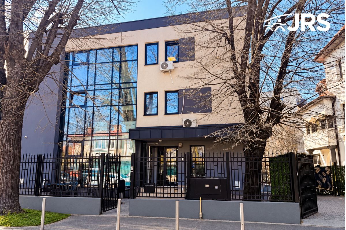 JRS Romania headquarters in Bucharest, with a glass facade, a metal fence and trees in front of the building.
