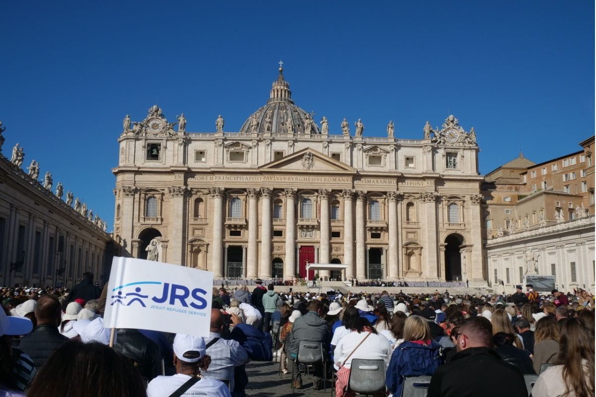 A white flag bearing the JRS logo among a crowd in front of St Peter’s Basilica in Vatican City.